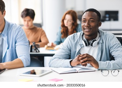 Back To Highschool. Portrait Of Interested Black Student Sitting At Desk With Multicultural Classmates, Listening To Teacher. Diverse People Studying And Learning New Stuff, Selective Focus