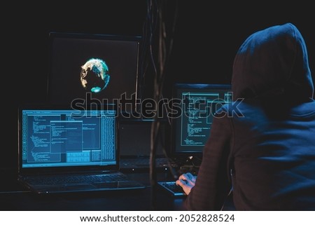 Back hooded hacker using malicious software hack corporate data center. malefactor hidden underground in dark place, multiple displays with phishing code and global map attack.
