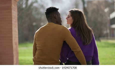 Back of interracial couple kissing sitting at park bench - Powered by Shutterstock