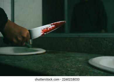 The back of a knife-wielding murderer in a dark bathroom looks grim as he is about to injure the horror victim of a bloodthirsty killer holding a large, bloody kitchen knife in his hand.
