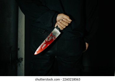 The back of a knife-wielding murderer in a dark room looks grim as he is about to injure the horror victim of a bloodthirsty killer who holds a large, bloody kitchen knife in his hand.