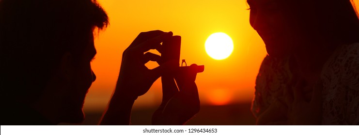 Back Light Banner Of Silhouette Of Marriage Proposal Offering Engagement Ring At Sunset