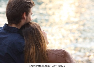Back light of a couple hugging and watching the sea at sunset on the beach