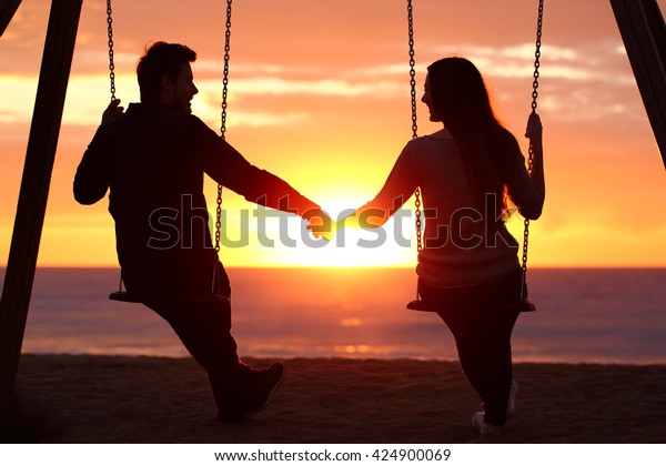 暖かい背景に日の出を見ながら手を振りながら座る夫婦のシルエットのバックライト の写真素材 今すぐ編集