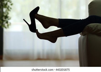 Back light silhouette of a woman resting with feet taking off shoes on a couch at home with a window in the background - Powered by Shutterstock