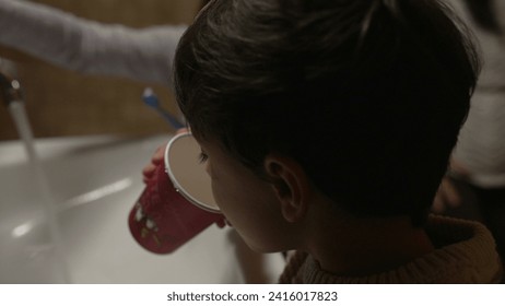 Back of little boy drinking water by sink after brushing teeth, child spitting toothbrush and hydrating himself - Powered by Shutterstock