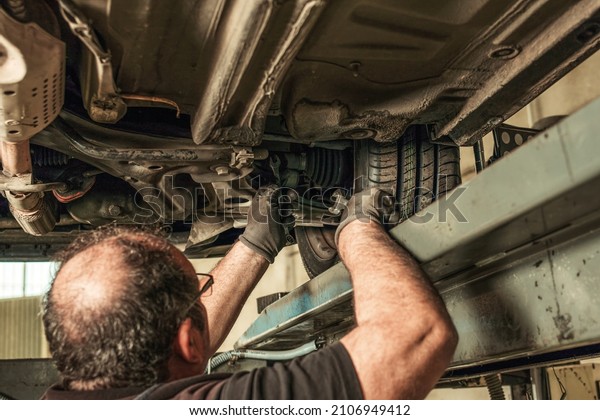 Back of a man under a car fixing steering\
alignment in a garage
