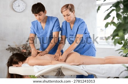 Back massage in four hands simultaneously - two professional masseurs treating young woman