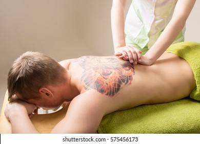 Back Massage. Massage Therapist Massaging Lower Back Region Of A Tattooed Man