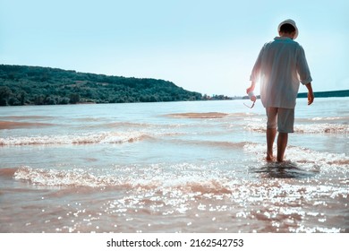 Back of mature Man walking on beach water on sunny day. Handsome man in a tropical beach wearing white shirt and sun hat. Copy space - Powered by Shutterstock