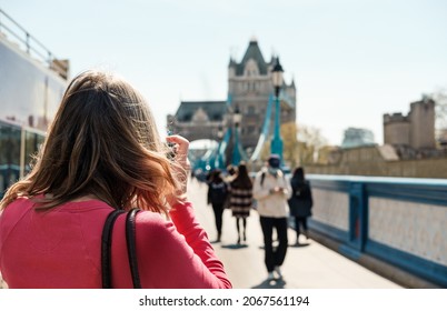 Back Of A Mature Woman Taking A Picture Of The Tower Bridge. People Is Walking Around.