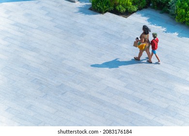 Back Of Mother And Child Walk Across On Concrete Pavement In Sunny Day. Family People Walking In The Street. Summer Season Of Crowd Life. (wide Angle Of Aerial Top View)