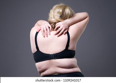 Back and neck pain, fat woman with backache, overweight female body on gray studio background