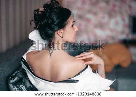 Back neck tattoo of a woman brunette girl in shirt at home