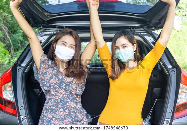 back to normal\
life or end of covid-19 , Coronavirus quarantine stop concept with\
two happy Asian woman wearing mask sitting on car and ready to\
travel with new normal lifestyle\
