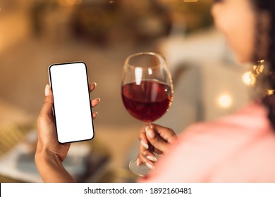 Back Over The Shoulder Back View Of Young Black Woman Holding And Using Mobile Phone With White Empty Screen For Mock Up, Making Virtual Call Or Watching Video, Drinking Red Wine From Glass - Powered by Shutterstock