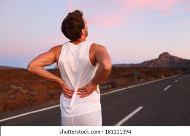 Back Pain. Athletic Running Man With Injury In Sportswear Rubbing Touching Lower Back Muscles Standing On Road Outside At Night.