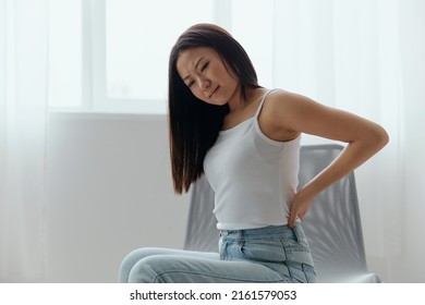 Back Pain. Suffering From Osteochondrosis After Long Study Work Pretty Young Asian Woman Touching Painful Lower Back At Home Interior Living Room. Injuries Poor Health Illness Concept. Cool Offer