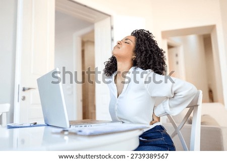 Back pain at work. Lower backache, People with body-muscles problem, Healthcare And Medicine concept. Attractive woman sitting at desk and holding painful lower back with hand while using her laptop.