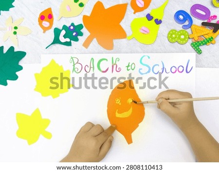 Back to School’ paintbrush text.  Child getting ready to create a greeting card.  On the table typical crafting materials. Showcases creativity, DIY, and craft activities. School supplies, art projects, educational content. Educational content about arts and crafts.