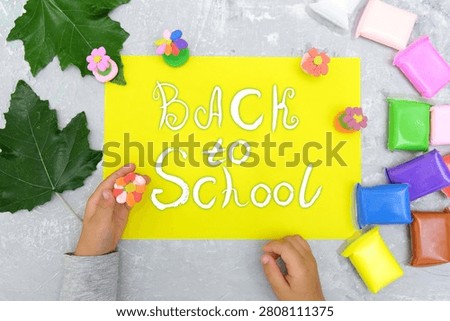 Back to School’ paintbrush text.  Child getting ready to create a greeting card.  On the table typical crafting materials. Showcases creativity, DIY, and craft activities. School supplies, art projects, educational content. Educational content about arts and crafts.