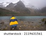 Back of a person crouching on the shore of a lake with snowy peaks on the background. Chacas, Peru