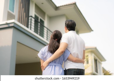 Back Portrait Of Asian Young Couple Standing And Hugging Together Looking Happy In Front Of Their New House To Start New Life. Family, Age, Home, Real Estate And People Concept.
