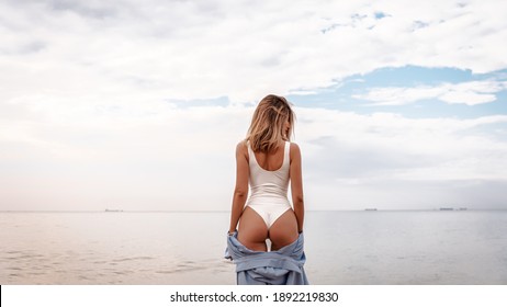Back portrait girl in swimwear posing at the beach, Tanned young woman in swimsuit posing in sea water among rocks, blonde girl at the beach, body, attractive, pretty, make up, model, hairstyle