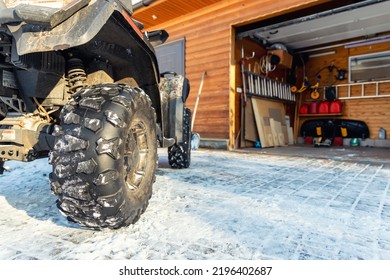 Back POV Close-up Detail View Of Quad Bike Offroad Vehicle Parked Front House Garage Open Door On Sunny Snowy Cold Winter Day. ATV Adventure Extreme Sport. Scoop Snow Removal Tool Eqiopment At Home