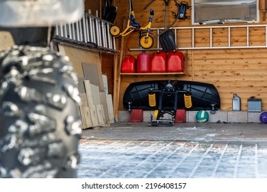 Back POV Close-up Detail View Of Quad Bike Offroad Vehicle Parked Front House Garage Open Door On Sunny Snowy Cold Winter Day. Scoop Snow Removal Tool Equipment At Home. Organized Stuff Storage Shed