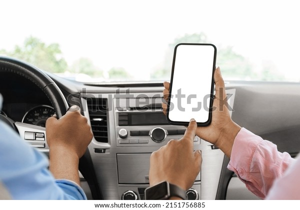 Back rear over the shoulder view of black female
passenger holding cell phone pointing finger at white blank screen
for mock up, sitting on front seat in car. Couple using app for
navigation, closeup