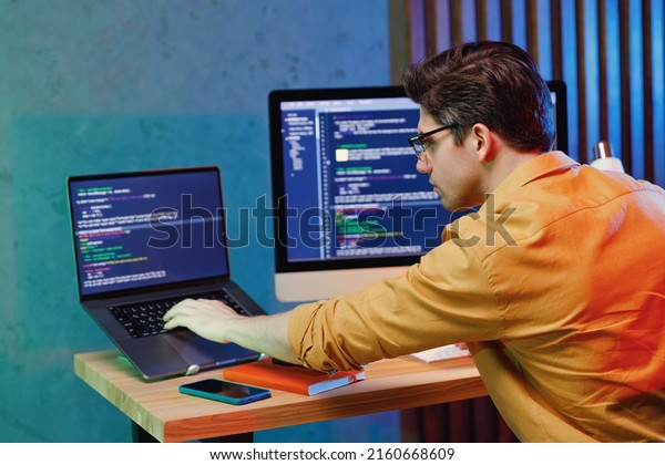 Back rear side profile view young data scientist\
software engineer IT specialist programmer man wearing shirt work\
at home writing typing code script on laptop pc computer. Game\
development concept