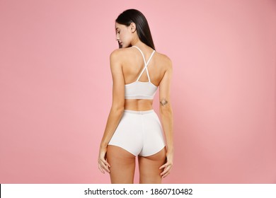 Back Rear View Of Beautiful Seductive Sexy Young Brunette Woman 20s In White Underwear Posing Hold Hands On Hips Legs Looking Down Isolated On Pastel Pink Colour Background, Studio Portrait