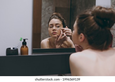 Back rear view disappointed half naked topless young woman 20s playing with her face squeeze pimple reflected in mirror in bathroom do morning routine Skin care healthcare cosmetic procedures concept