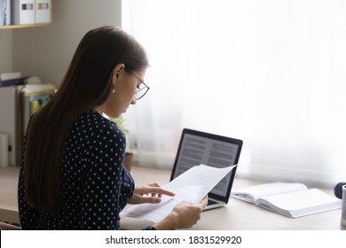 Back rear view focused young woman in eyeglasses reading paper document, checking electronic report on computer. Concentrated smart ambitious businesswoman preparing research, freelance work. - Shutterstock ID 1831529920