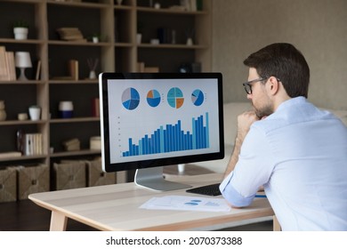 Back rear view focused young businessman looking at computer monitor, analyzing project statistics, marketing research results or statistics data, developing marketing strategy, working at home office - Shutterstock ID 2070373388
