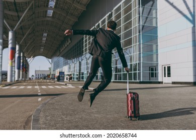 Back rear view full length young traveler businessman man wearing black dinner suit stand outside at international airport terminal with suitcase valise jumping high Air flight business trip concept.