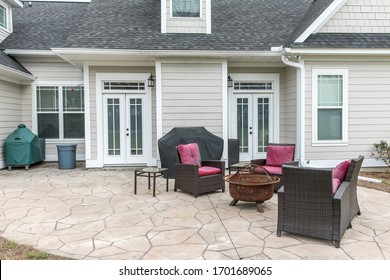 The back rear view of a new construction home with a covered up barbecue and patio furniture with a stamped concrete patio floor - Shutterstock ID 1701689065