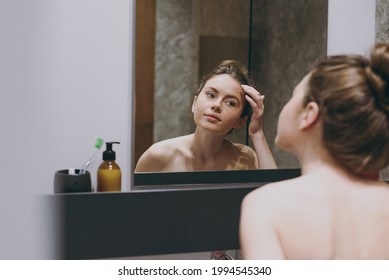 Back rear view nice half naked topless caucasian young woman 20s touching forehead reflected in mirror in bathroom doing morning routine. Skin care healthcare cosmetic procedures lifestyle concept.