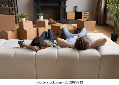 Back rear view tired young family couple lying on comfortable sofa, resting after hard moving day near huge carton boxes. Satisfied new homeowners relaxing on couch in modern renovated living room. - Powered by Shutterstock