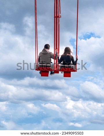 Back rear view of tourist couple on red seesaw swinging high in the air space against beautiful blue sky above the town. Amsterdam, Holland.