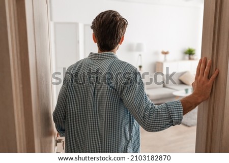 Back rear view of unrecognizable young man walking in his apartment, entering new home, casual guy standing in doorway of modern flat, looking at design interior, coming inside, selective focus