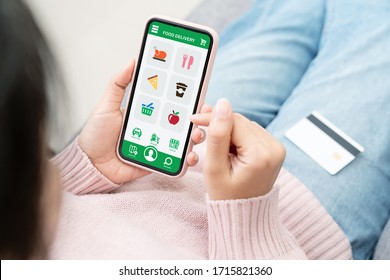 Back Rear View Of Young Asian Teenage Girl In Concept Next Normal Life From Coronavirus Impact Using Smart Phone On Hand And Pay By Credit Card At Home. Food Delivery Or Grocery Order Service At Home.