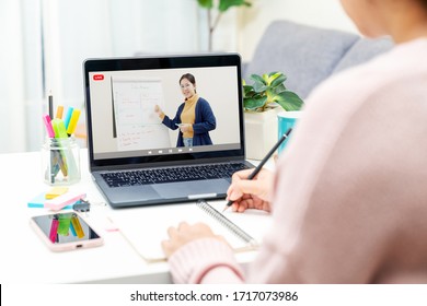 Back Rear View Of Young Asian Girl Sit On Desk And Learn At Home Living Room In Concept Of Romote Learning, Virtual Online, Self Isolated Quarantine Lifestyle In Asia. Teaching Video Call On Computer.