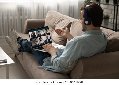 Back rear view young businessman employee in headphones holding video conference online meeting with mixed race colleagues, discussing working issues remotely from home, lying on comfortable sofa. - Shutterstock ID 1859118298