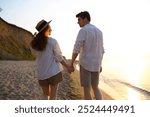 Back rear view young couple two friends family man woman in white shirt clothes hold hands look to each other walk together at sunrise over sea beach ocean outdoor exotic seaside in summer day evening