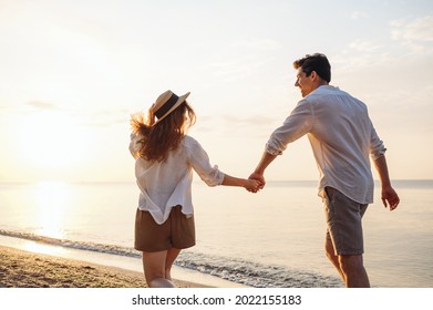 Back rear view young happy couple two friends family man woman in white shirt clothes hold hands walk run stroll together at sunrise over sea beach ocean outdoor exotic seaside in summer day evening - Powered by Shutterstock