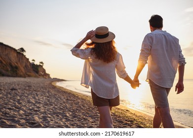 Back rear view young lovely couple two friends family man woman wearing casual clothes hold hands walking stroll together at sunrise over sea beach ocean outdoor exotic seaside in summer day evening