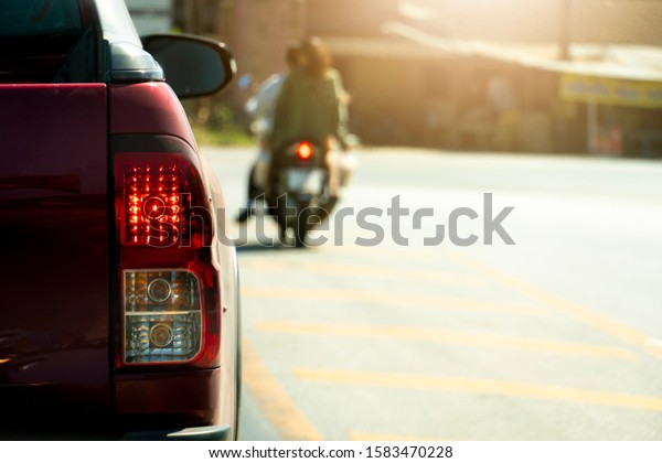 The back of a red pick-up\
truck stop and open brake light on the road with blurred of\
motorcycle.