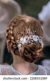 Back of redhead flower girl with hair in a bun and braids, decorated with flowers, butterflies and pearls. - Shutterstock ID 2208551089